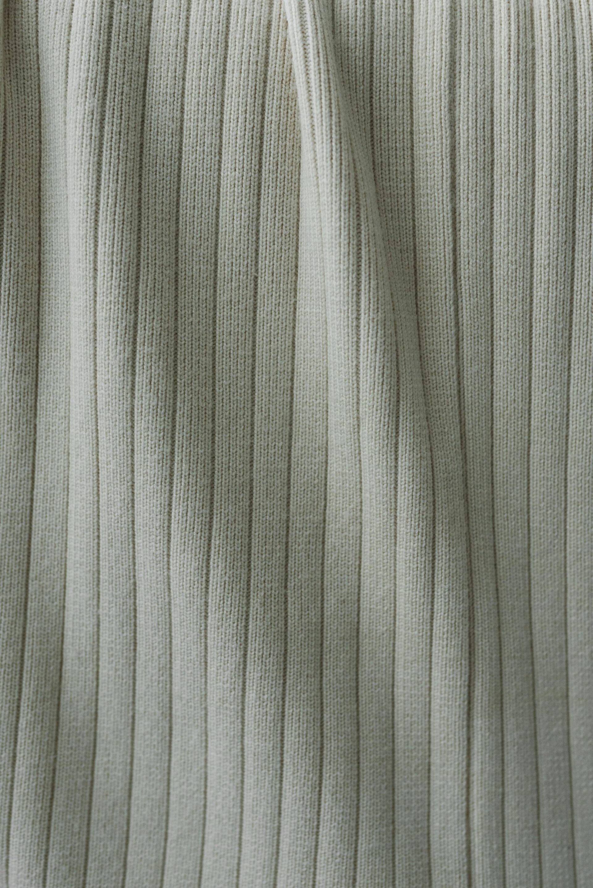 Detailed view of high-density vertical ribbed flat knit fabric in a soft cream finish.
